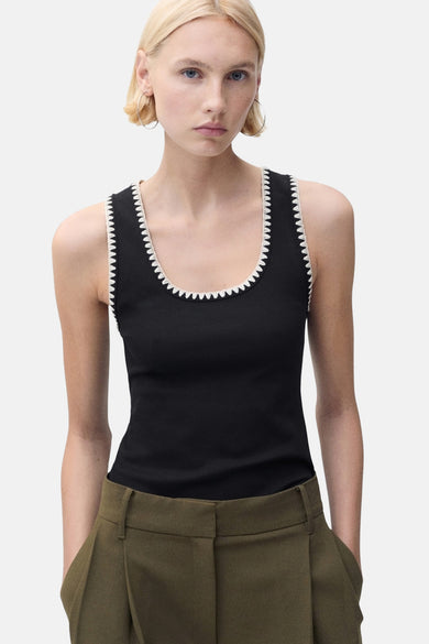 Débardeur noir de MANGO, avec bordure festonnée blanche, porté avec un pantalon ample vert olive.
