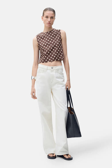 Blouse marron à pois blancs de MANGO, portée avec un jean blanc et un sac noir.