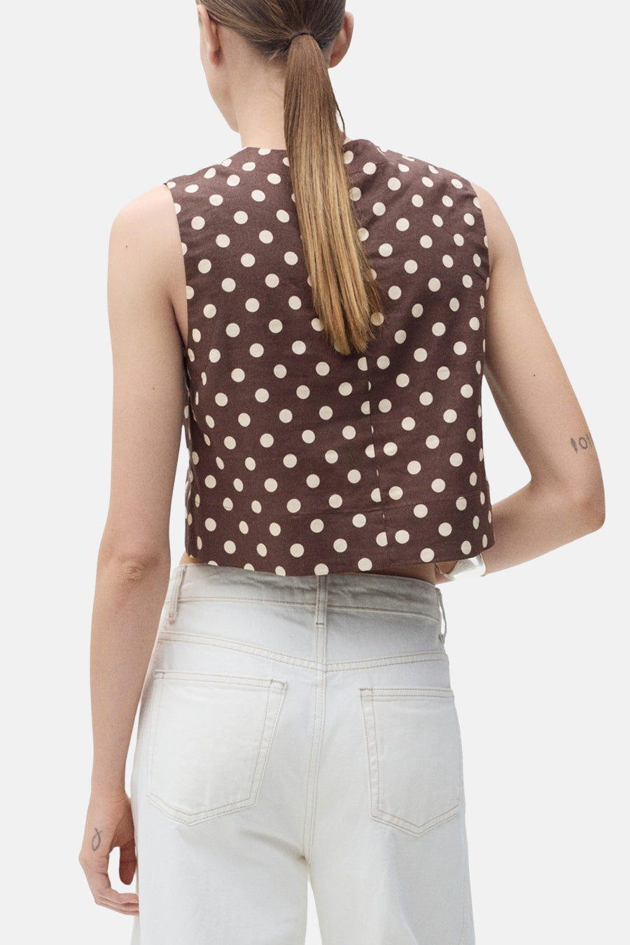 Blouse sans manches marron à pois, de MANGO, portée avec un jean blanc taille haute.
