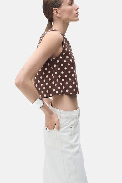 Blouse sans manches marron à pois, de MANGO, portée avec un bracelet argenté et une jupe blanche.