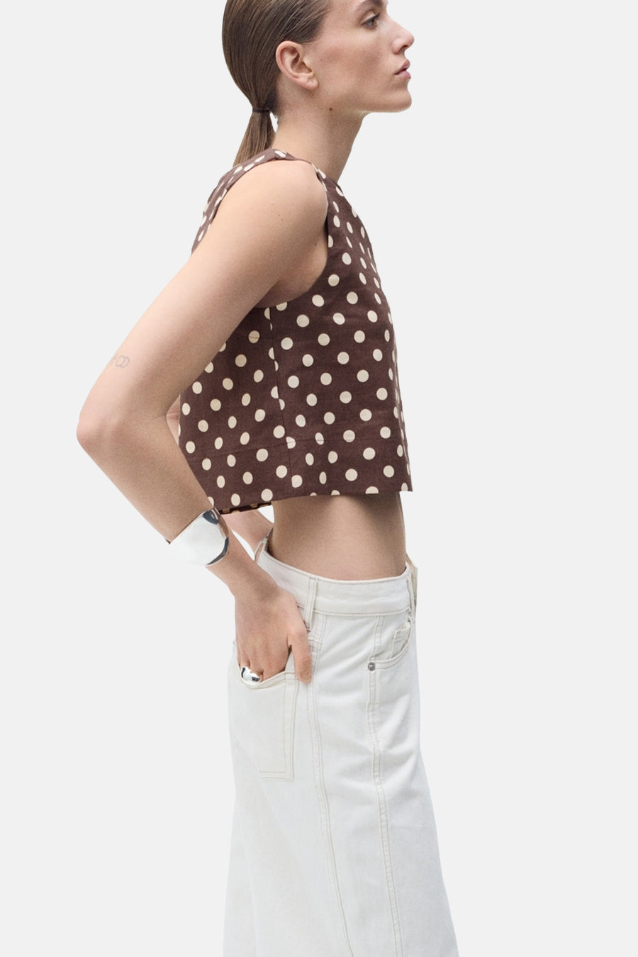 Blouse sans manches marron à pois, de MANGO, portée avec un bracelet argenté et une jupe blanche.
