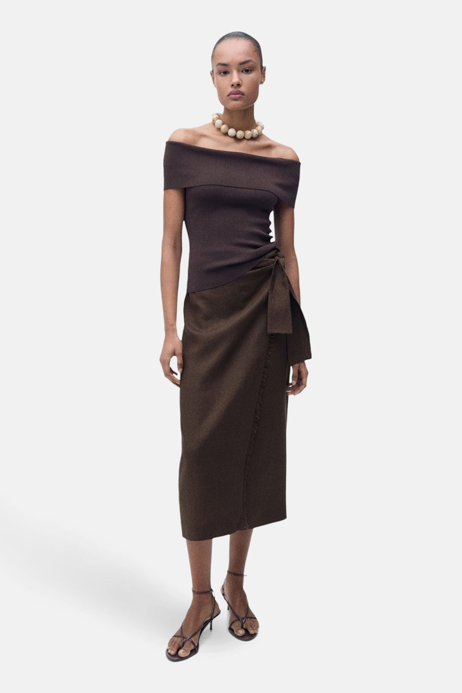 Jupe 3/4 marron, de MANGO, avec détail noué sur le côté, portée avec un top et un collier beige.
