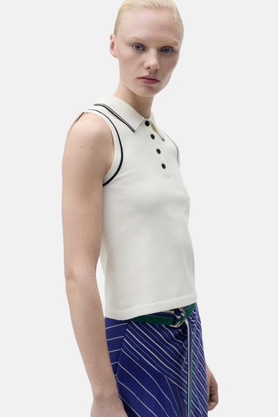 Polo blanc à manches courtes de MANGO, avec des bordures noires et porté avec une jupe rayée bleue et blanche.
