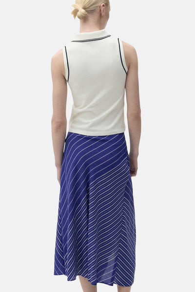 Polo blanc à col, de MANGO, avec bordures noires, porté avec une jupe longue rayée bleue et blanche.