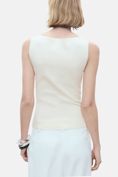 Ecru hemdje van MANGO, met een aansluitende pasvorm, gedragen met een witte broek en een zilveren armband.