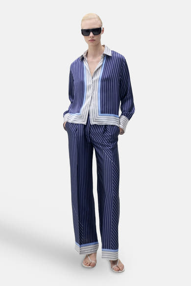 Blauw gestreept overhemd met lange mouwen van MANGO, gedragen met een bijpassende broek en een zwarte zonnebril.