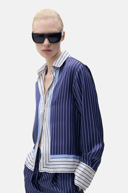 Blauwe gestreepte blouse met lange mouwen van MANGO, gedragen met een andere gestreepte blouse en een zwarte zonnebril.