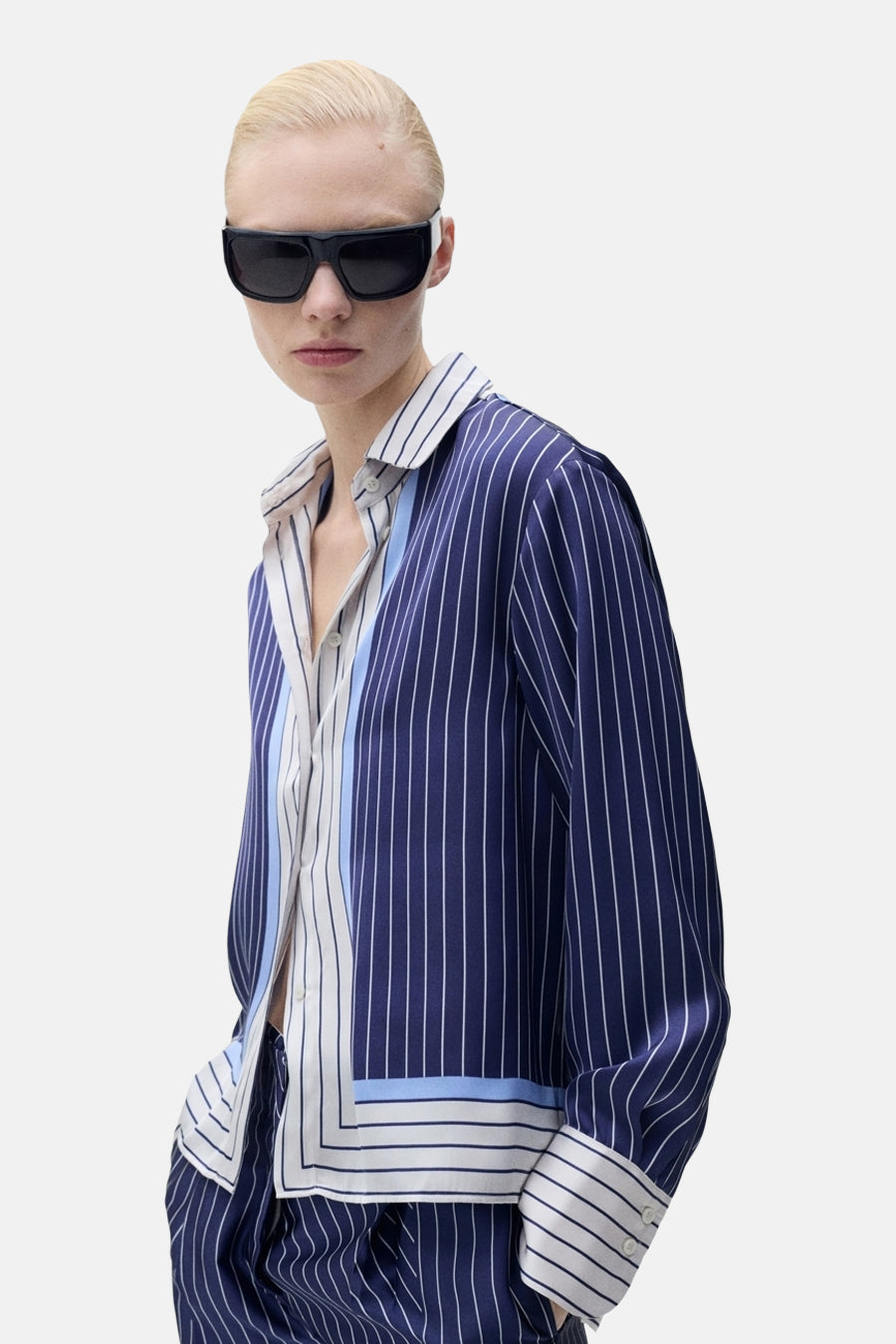 Blauwe gestreepte blouse met lange mouwen van MANGO, gedragen met een andere gestreepte blouse en een zwarte zonnebril.