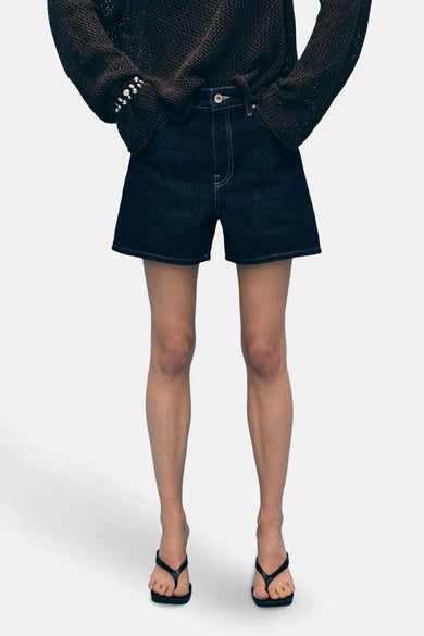 Donkerblauwe denim bermuda van MANGO, achterkant, met contrasterende stiksels en gedragen met een oversized bruine trui.