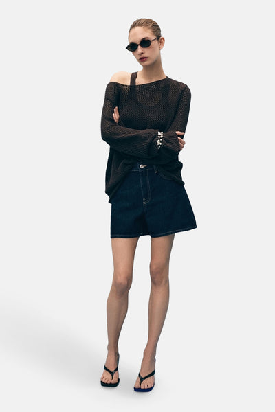 Donkerblauwe denim bermudashorts van MANGO, gedragen met een losgebreide trui en sandalen met bandjes.