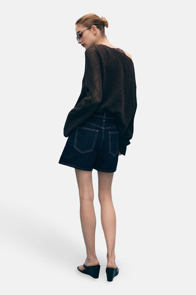 Bermuda en denim bleu foncé de MANGO, vue de dos, avec coutures contrastantes et portés avec un pull ample marron.
