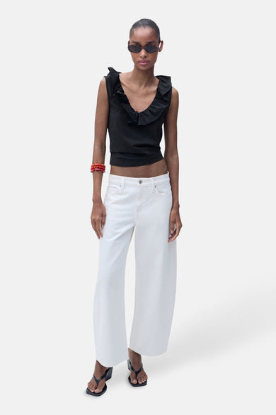 Top sans manches noir de MANGO, avec volant à l'encolure, porté avec un pantalon blanc et des sandales.