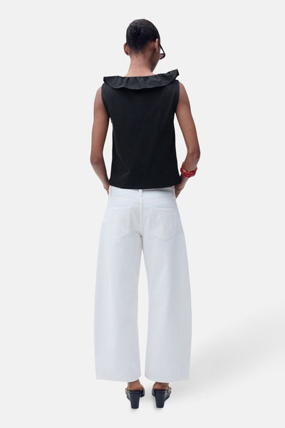Top sans manches noir de MANGO, avec une encolure à volant, porté avec un pantalon blanc ample et des sandales à talons.