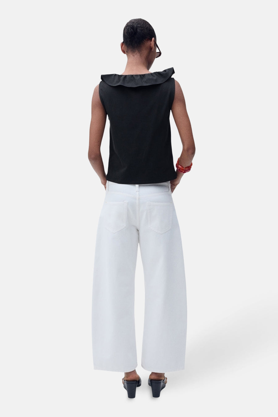 Zwart mouwloos topje van MANGO, met een volant halslijn, gedragen met een wijde witte broek en sandalen met hak.
