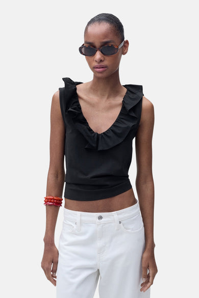 Top noir sans manches de MANGO, orné de volants, porté avec un jean blanc et un bracelet rouge.