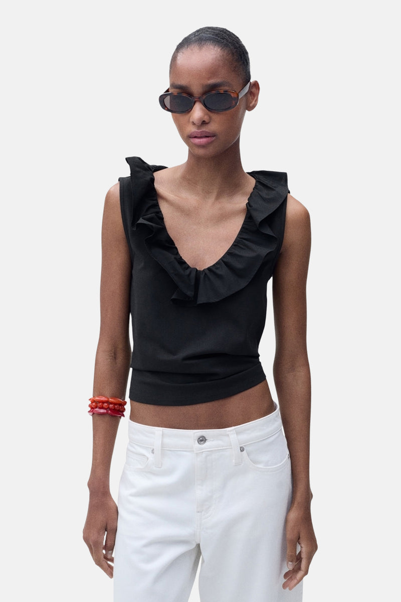 Top noir sans manches de MANGO, orné de volants, porté avec un jean blanc et un bracelet rouge.