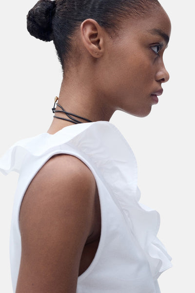 Top sans manches blanc de MANGO, avec volant décoratif sur l'épaule, porté avec un collier à cordons.