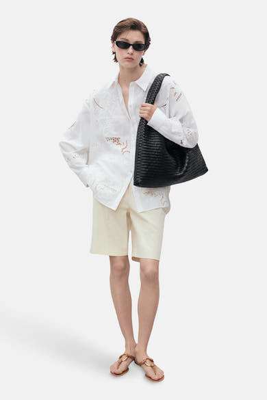 Wit overhemd met lange mouwen van MANGO, met bloemenborduursels en gedragen met een beige korte broek en sandalen.