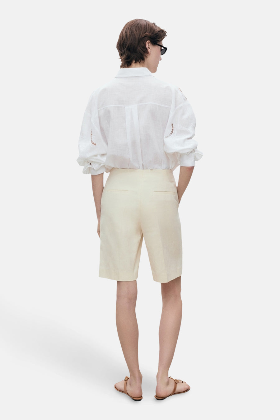 Chemise à manches longues blanche MANGO, avec détails ajourés, portée avec un short beige et des sandales marron.
