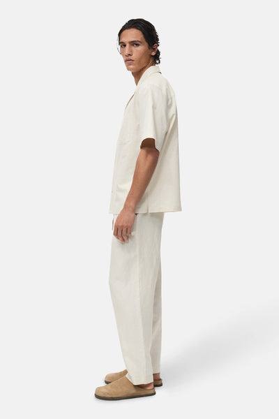 Chemise écru à manches courtes de MANGO, portée avec un pantalon assorti et des sabots en daim, vue de profil.