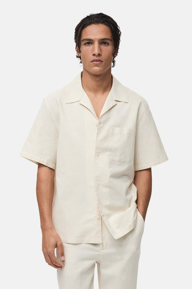Ecru overhemd met korte mouwen van MANGO, gedragen met een bijpassende broek en suède klompen, van opzij gezien.