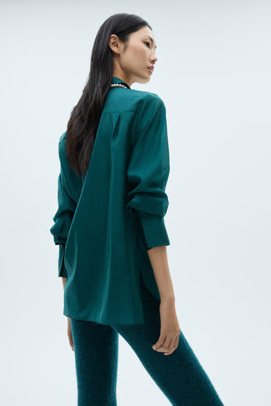 Turquoise blouse met lange mouwen van MANGO, met een parelketting en bijpassende legging.