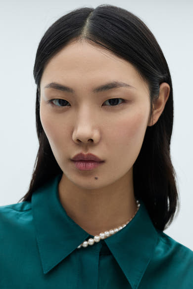 Turkooizen blouse met lange mouwen van MANGO, gedragen met een parelketting.
