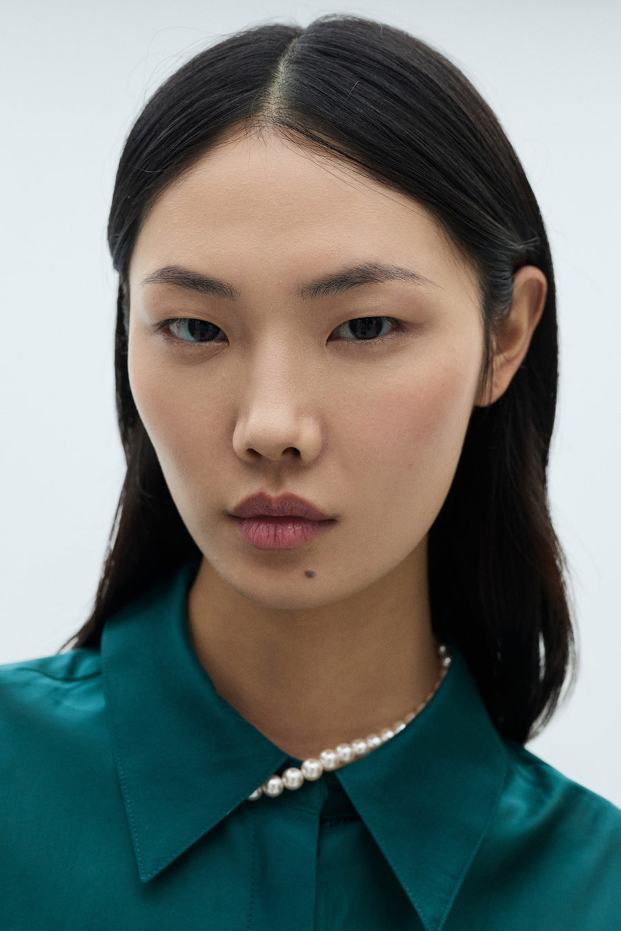 Turkooizen blouse met lange mouwen van MANGO, gedragen met een parelketting.