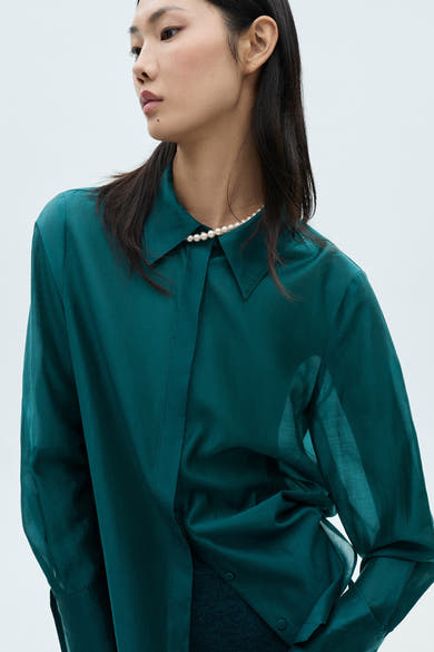 Turquoise blouse met lange mouwen van MANGO, met parelketting en licht doorschijnende stof.