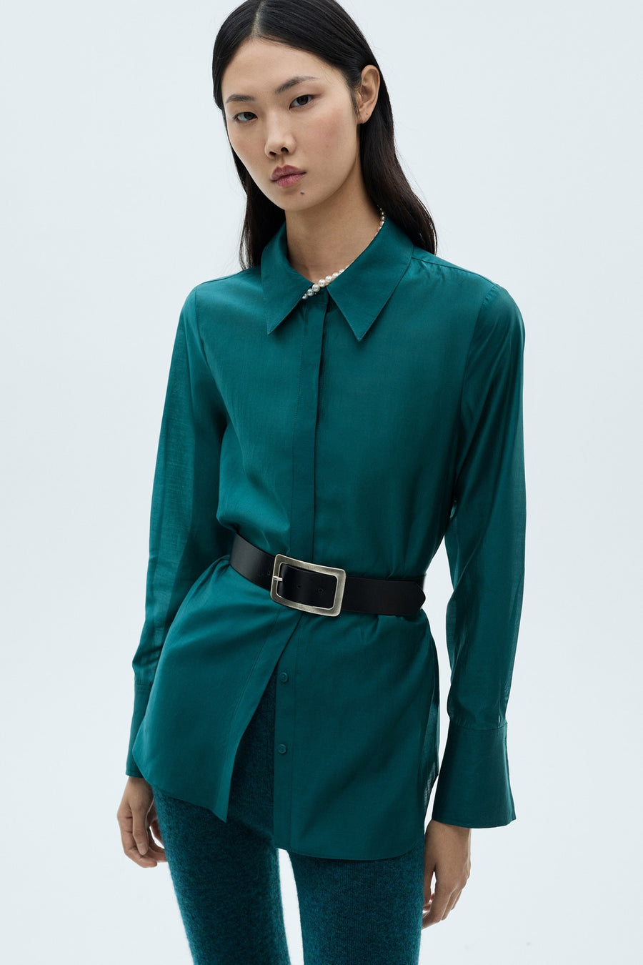 Turquoise overhemd met lange mouwen van MANGO, met een zwarte riem met zilveren gesp en een parelketting.