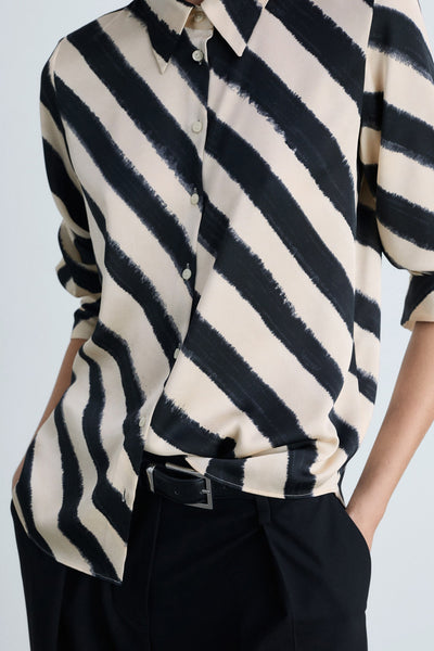 Chemise à manches longues noire et crème à rayures diagonales by MANGO, avec boutons et portée avec un pantalon noir.
