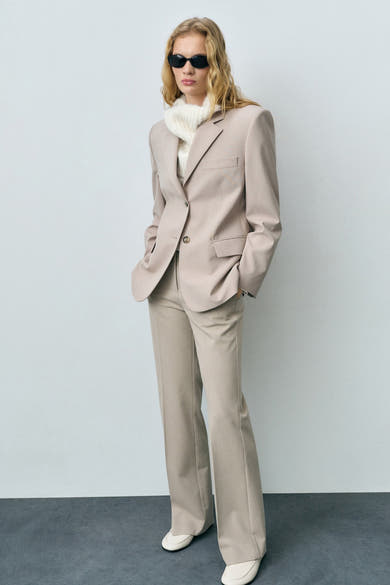 Pantalon de costume beige de MANGO, coupe droite, porté avec un pull en maille et des mocassins crème.
