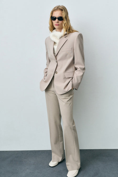 Beige kostuumbroek van MANGO, rechte pasvorm, gedragen met een gebreide trui en crèmekleurige loafers.