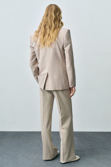 Pantalon de costume beige de MANGO, avec jambes larges et chaussures assorties, vu de dos.
