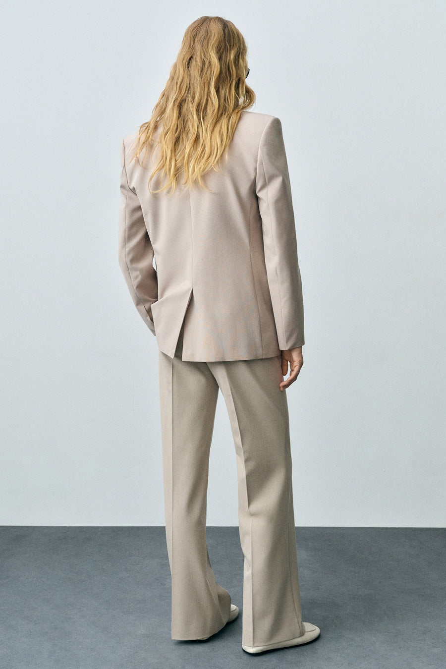 Pantalon de costume beige de MANGO, avec jambes larges et chaussures assorties, vu de dos.
