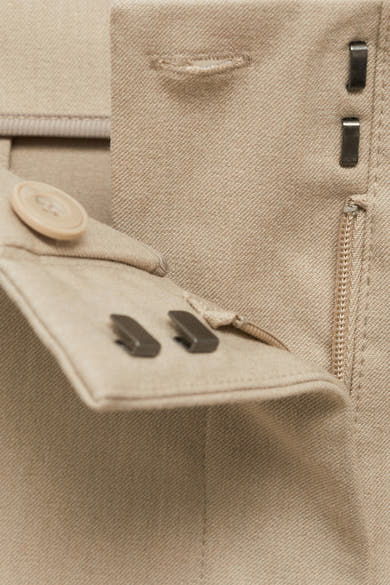Pantalon de costume beige par MANGO, avec fermeture éclair, agrafes et bouton apparents.