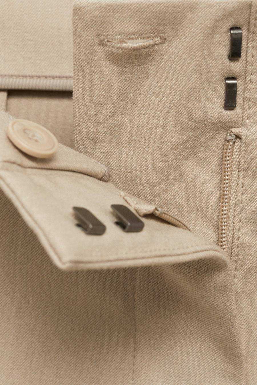 Pantalon de costume beige par MANGO, avec fermeture éclair, agrafes et bouton apparents.