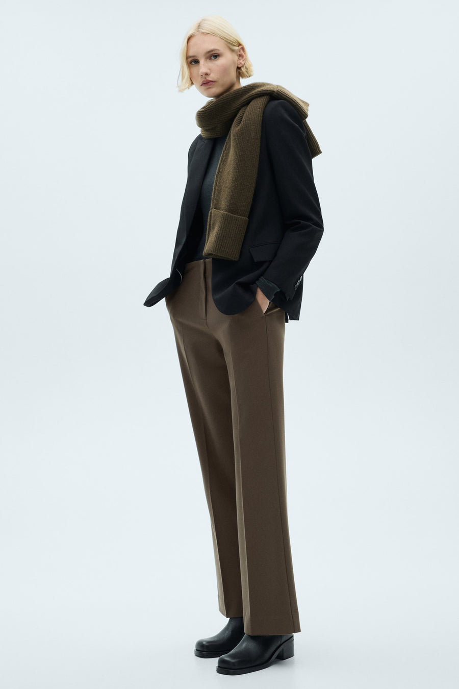 Pantalon de costume brun de MANGO, porté avec un blazer noir et une écharpe en laine.