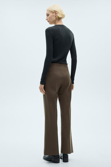Pantalon de costume brun de MANGO, coupe droite, porté avec un haut noir à manches longues et des chaussures noires.
