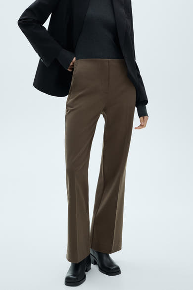 Pantalon de costume brun de MANGO, coupe droite évasée, porté avec un pull et une veste noirs.
