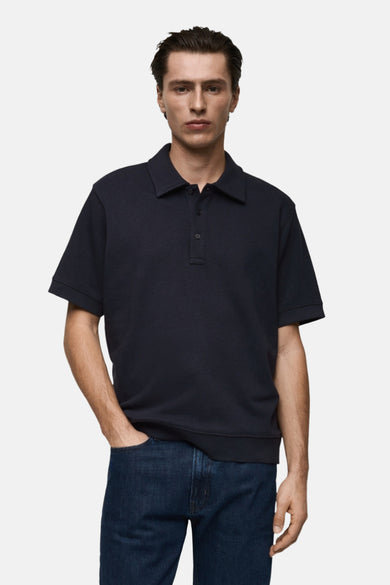 Polo bleu foncé en maille par MANGO, porté avec un jean, une main dans la poche.