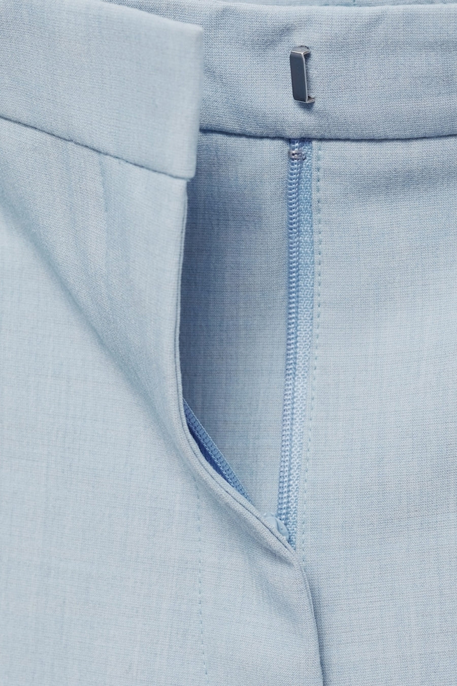 Lichtblauwe pantalon van MANGO, met een zichtbare ritssluiting en een subtiele textuur.