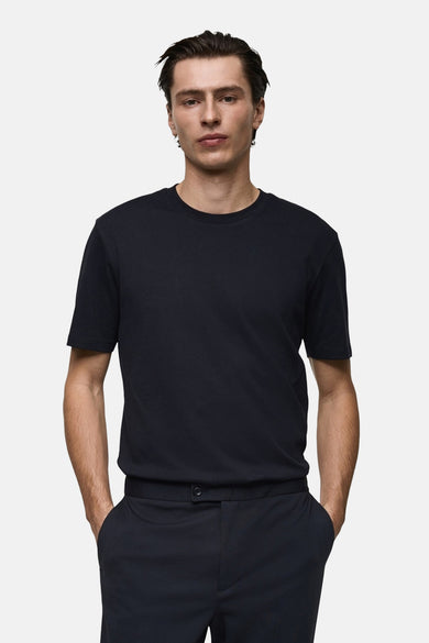 T-shirt bleu foncé à manches courtes de MANGO, porté avec un pantalon assorti, les mains dans les poches.
