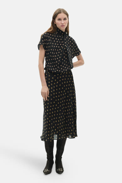 Jupe longue multicolore de MANGO, à pois beiges sur fond noir, portée avec des bottes en daim.
