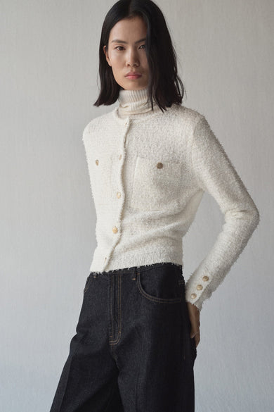 Witte gebreide bodywarmer van MANGO, met gouden knopen en gedragen over een ivoorkleurige coltrui.