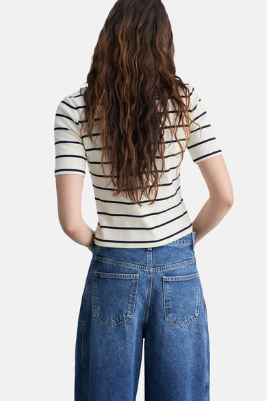 T-shirt rayé blanc à manches courtes de MANGO, porté avec un jean bleu taille haute, vue de dos.
