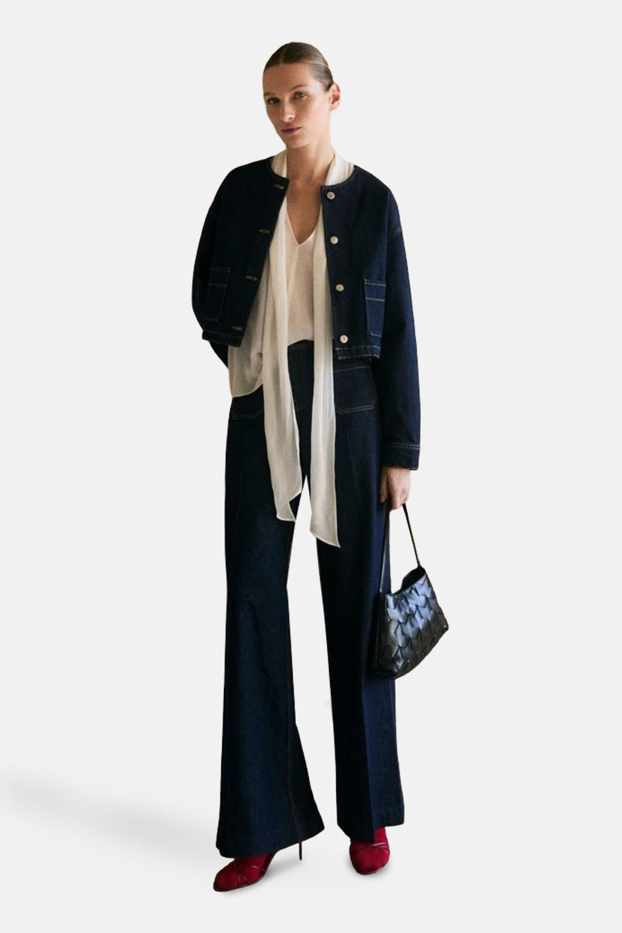 Blazer bleu moyen en denim par MANGO, porté sur un chemisier blanc et un pantalon évasé, avec un sac à main noir.
