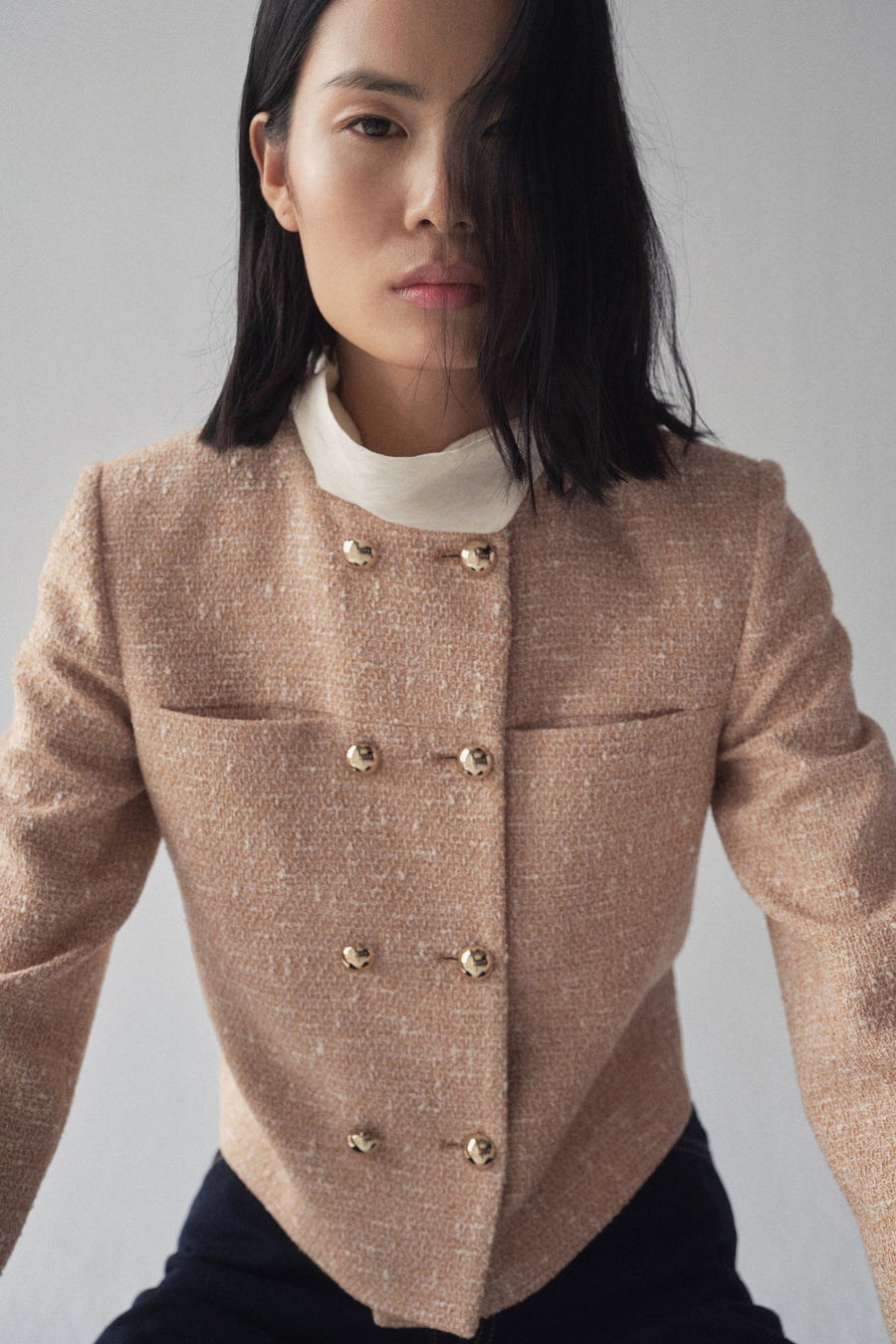 Beige tweed blazer van MANGO met gouden knopen en opgestikte zakken, gedragen met een witte top.