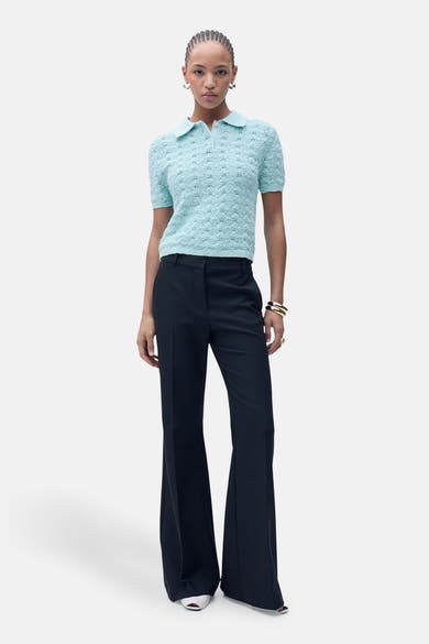 Polo bleu à manches courtes de MANGO, avec motif ajouré, porté avec un pantalon évasé et des bijoux dorés.
