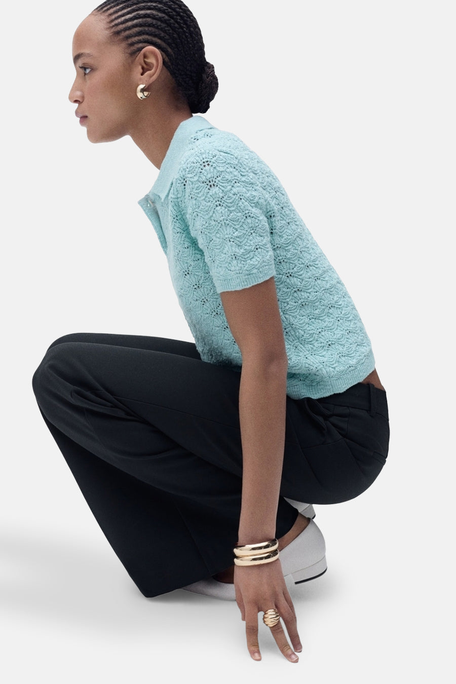 Polo bleu en maille ajourée de MANGO, porté avec un pantalon noir ample et des bijoux dorés.
